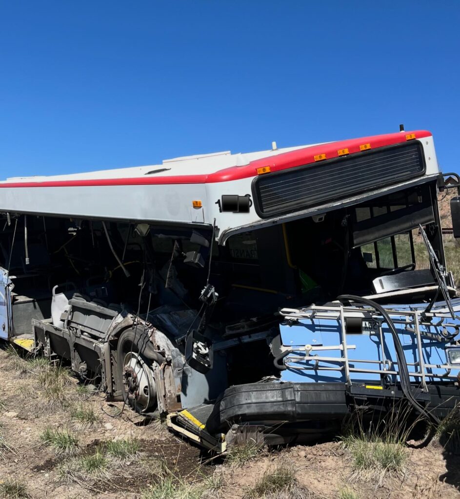 Autobús con daños severos en el costado y la parte frontal, fuera de la carretera tras un accidente en zona rural.